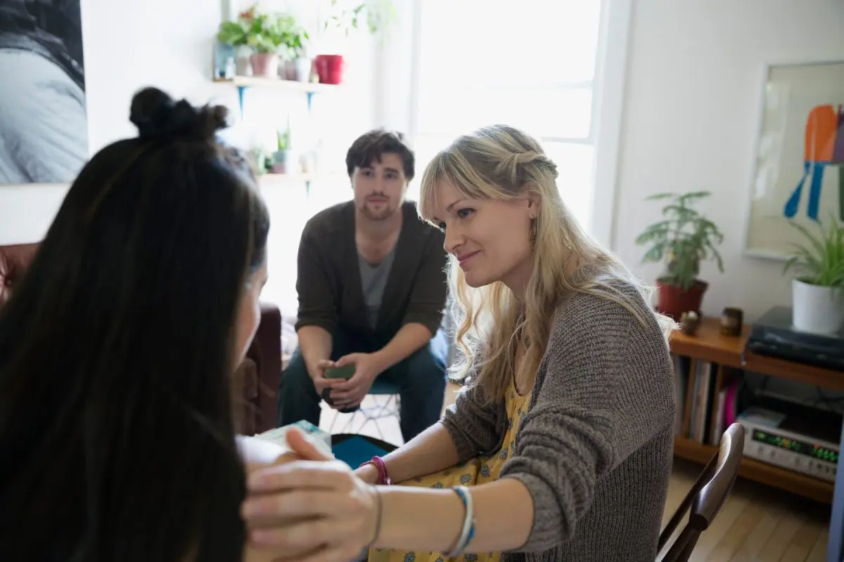 Three people having a heartfelt conversation in a cozy, plant-filled living room
