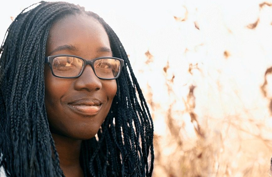 Smiling woman with braided hair and glasses outdoors in warm sunlight